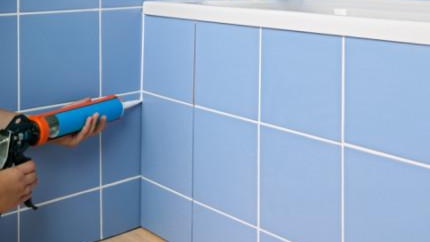 Mains appliquant du mastic sur le côté du bain